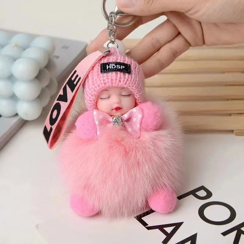 A pink fluffy cartoon plush doll keychain with a bow and a silver charm