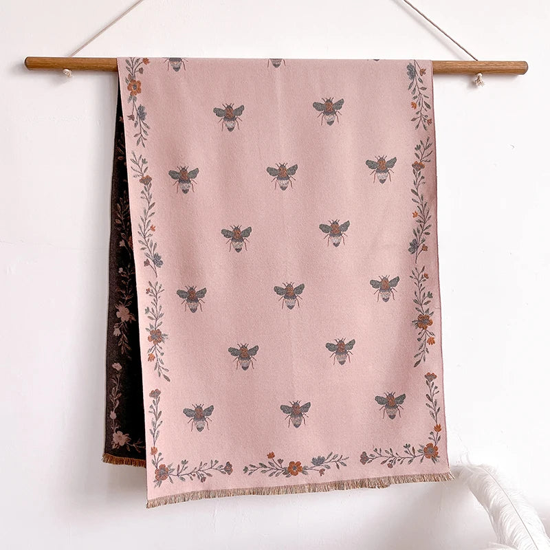 A pink pashmina shawl featuring a floral print of small bees and greenery.