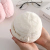 A hand holds a white plush fur ear warmer or earmuff against a light background.