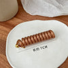 A copper-colored rubber braided ponytail holder, approximately 7cm long, resting on a white plate.