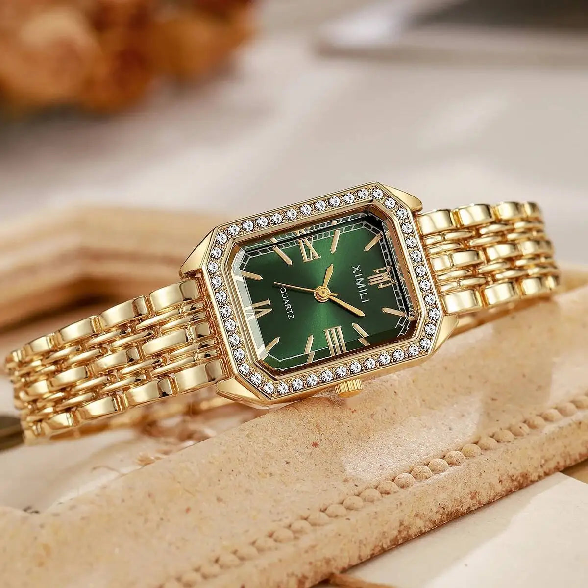 A gold-toned rhinestone quartz wristwatch with a green face and gold links is displayed on a light brown surface.