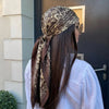 A woman with long dark hair wearing a brown and beige leopard print silk scarf and sunglasses.