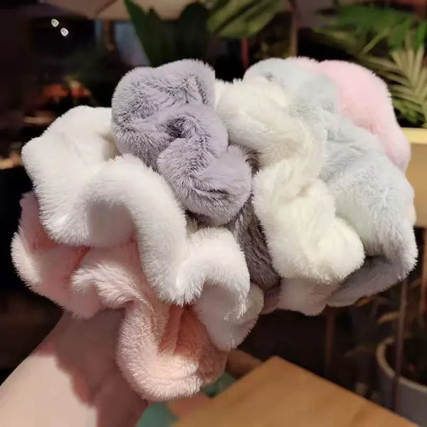 Una pila de gomas para el pelo de punto peludo en colores pastel, incluyendo rosa, blanco, lavanda y gris.