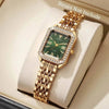 A gold-toned quartz wristwatch with a green face and rhinestone accents is displayed in a light-colored box.