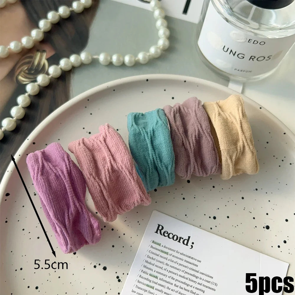 A collection of five pastel colored elastic hair bands for ponytails arranged on a white plate.