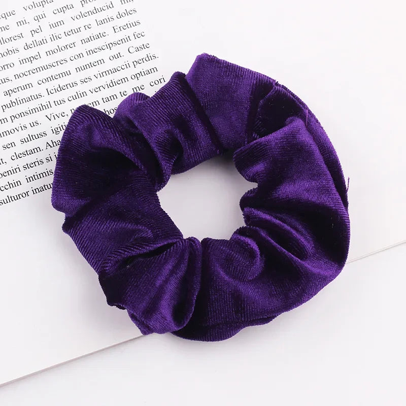 A close-up photo of a deep purple velvet scrunchie tied around a white piece of paper.