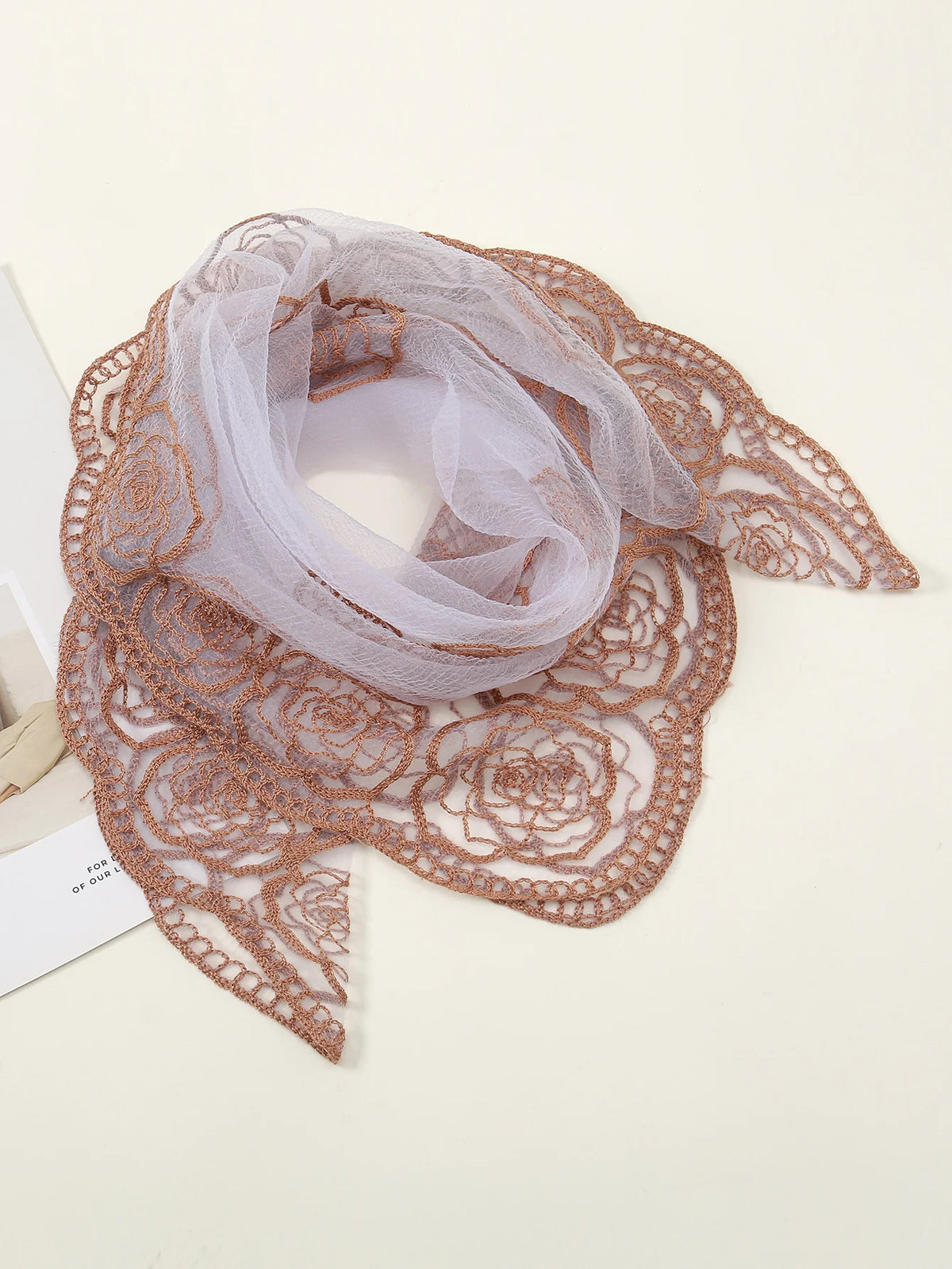 A close-up of a sheer, floral embroidered lace bandana headscarf in a warm brown tone.