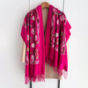A vibrant magenta floral scarf draped over a beige garment, featuring intricate embroidery and fringe.