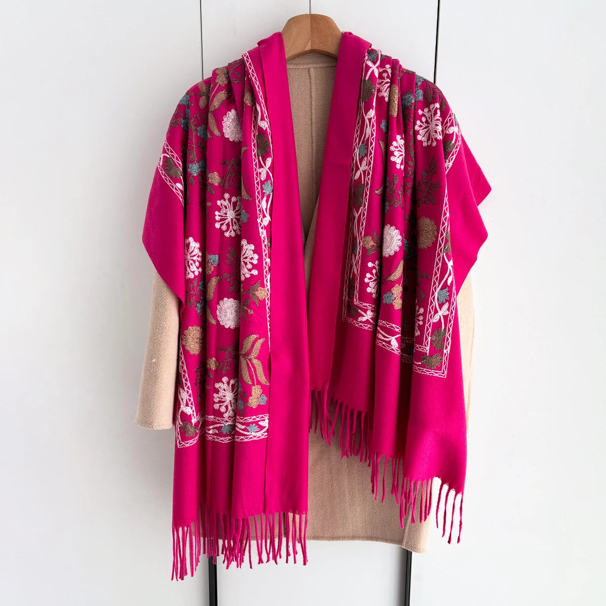 A vibrant magenta floral scarf draped over a beige garment, featuring intricate embroidery and fringe.