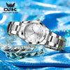 A silver luminous quartz watch is displayed on a blue fabric, resting on a clear glass surface.