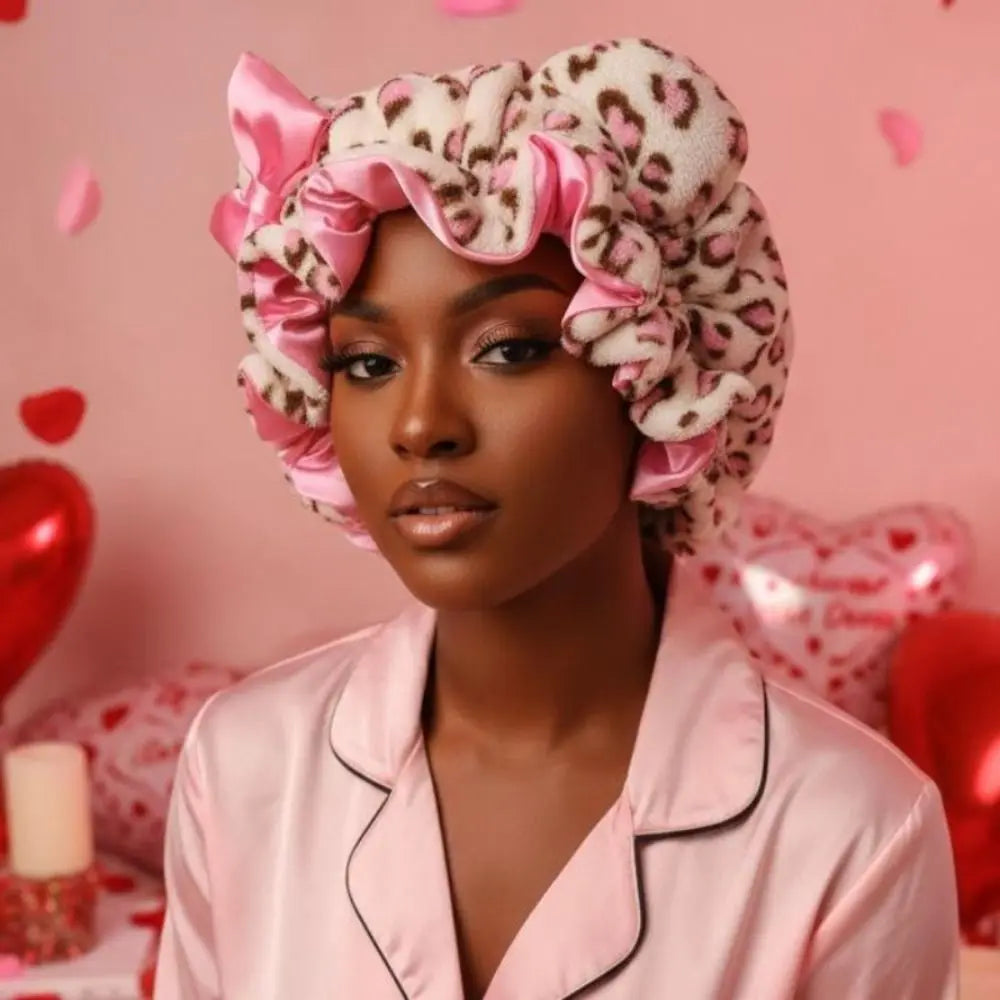 A woman wearing a pink leopard print hair drying cap against a pink background.