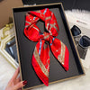 A vibrant red silk scarf tied in a bow displayed in a black frame on a white fluffy surface.