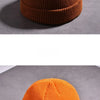 A close-up of a warm knitted beanie cap in a burnt orange color resting on a gray surface.