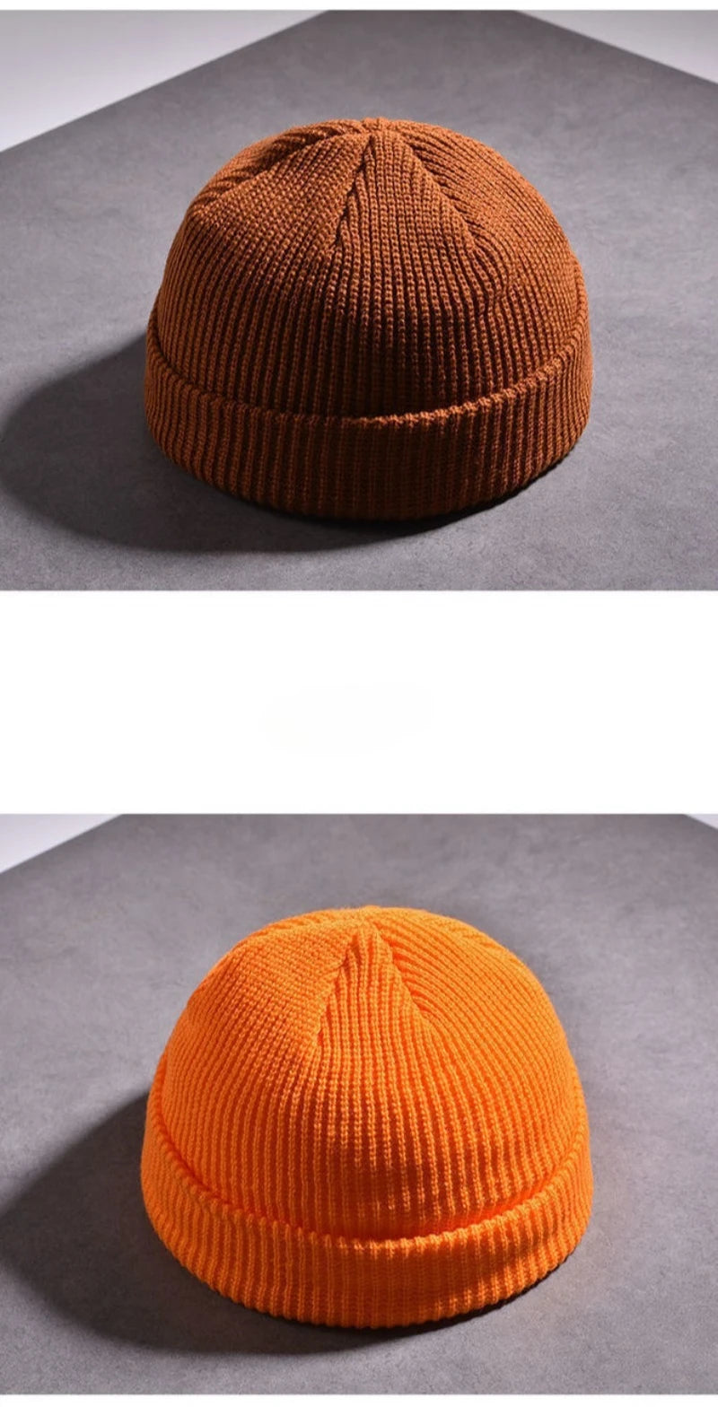 A close-up of a warm knitted beanie cap in a burnt orange color resting on a gray surface.
