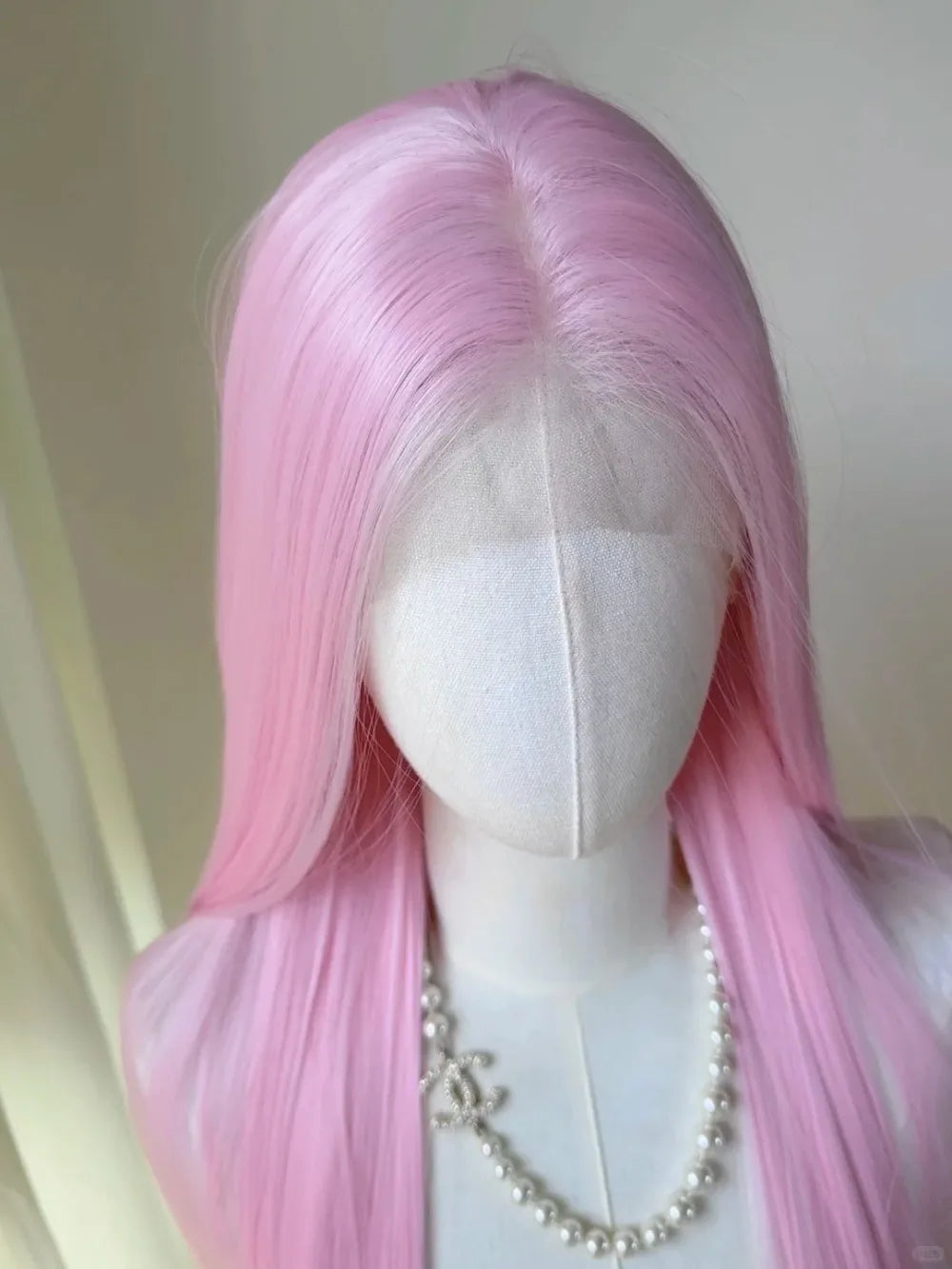 A long straight pink wig displayed on a mannequin, featuring a pearl necklace.