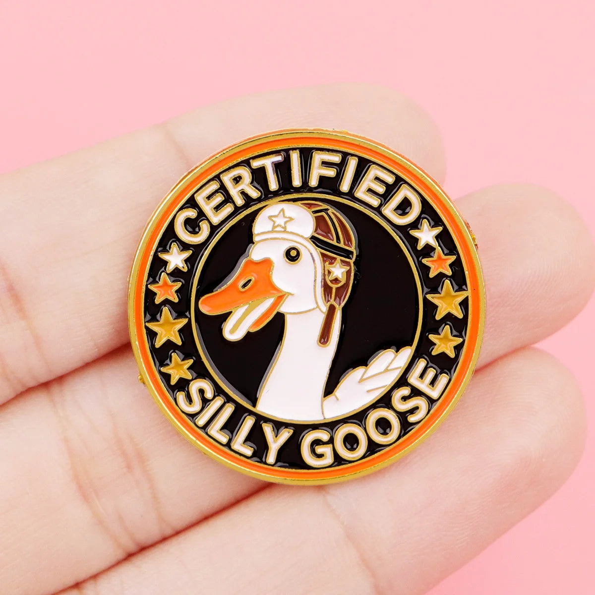 A gold-rimmed enamel pin featuring a white goose silhouette with a cap and stars, surrounded by text.