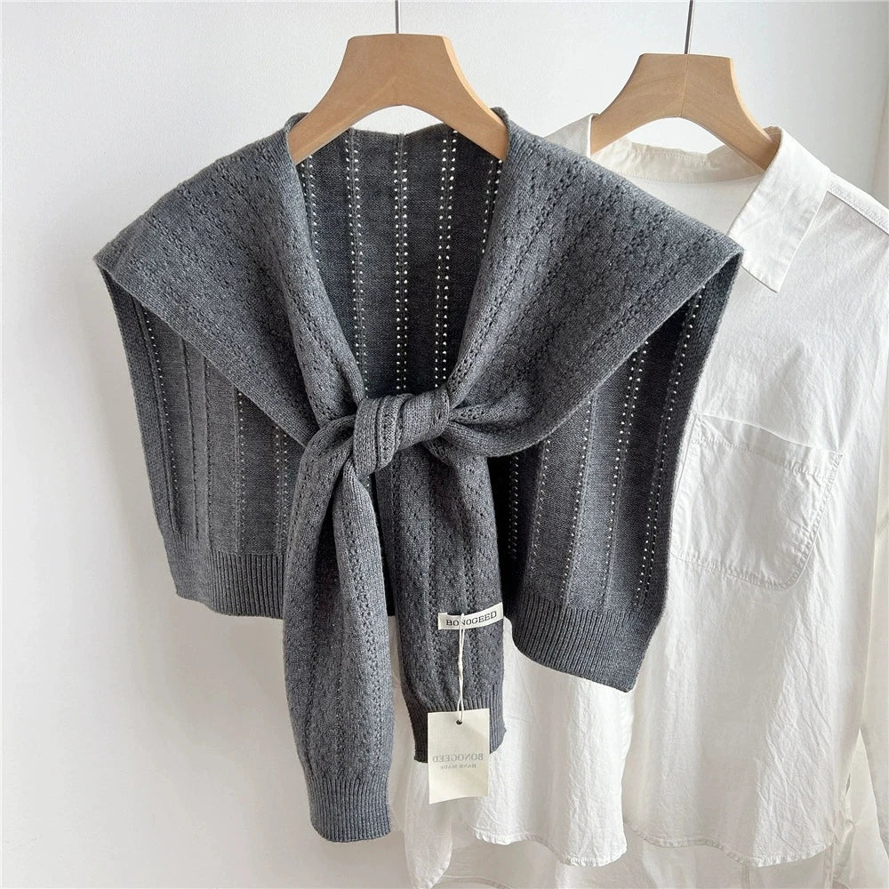 Chal de acrílico tejido gris doblado y exhibido en percha contra una camisa blanca.