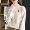 A close-up of a cream knit sweater with ribbed details and a small red flower pin on the chest.
