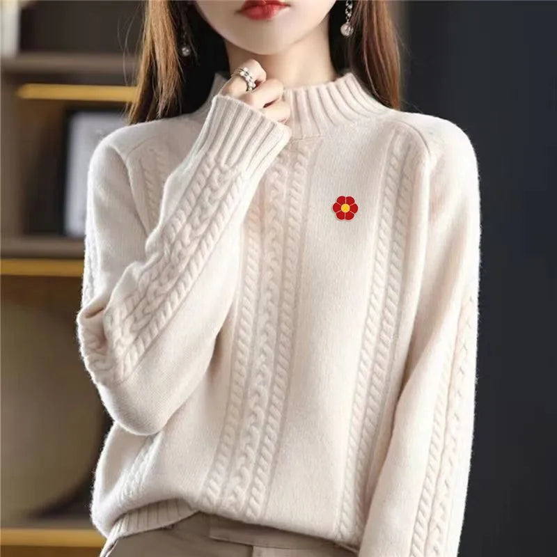 A close-up of a cream knit sweater with ribbed details and a small red flower pin on the chest.