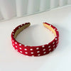 A red fabric hairband with white polka dots is displayed on a white surface.
