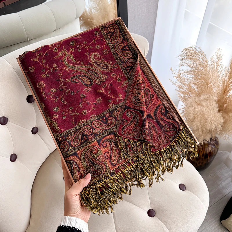 A deep red and gold bohemian paisley tassel shawl draped over a light colored sofa.