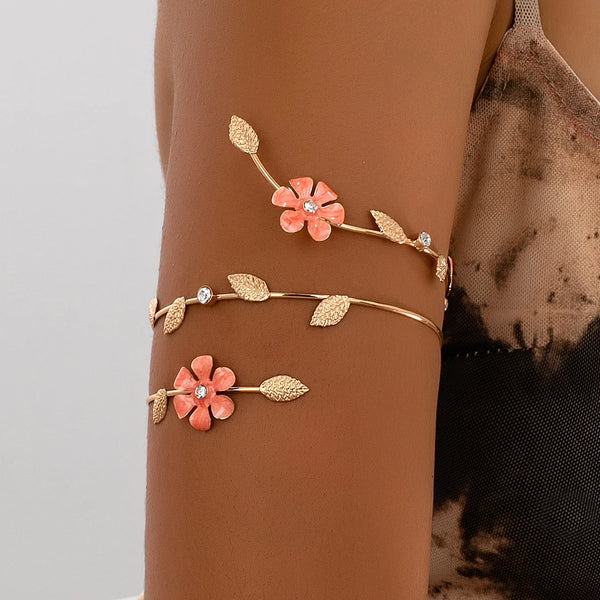 A close-up of a floral vine arm bracelet featuring pink flowers and gold leaves worn on a person's arm.
