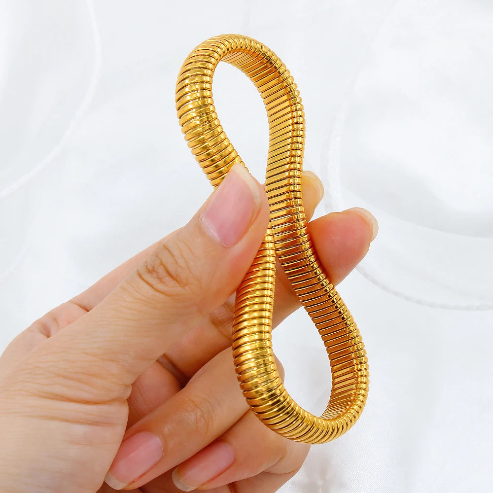 A hand holds a coiled 18k gold plated stainless steel elastic bangle bracelet.