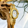 Un reloj vintage dorado con esfera blanca y bisel dorado junto a un trozo de madera flotante.
