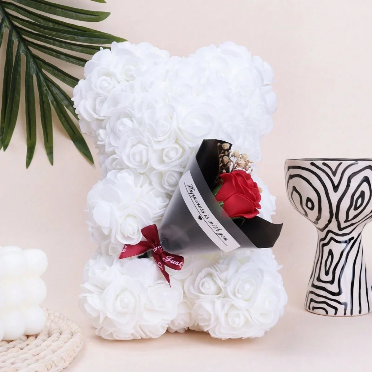 Bouquet de ours en peluche rose avec mousse blanche, ruban rouge et emballage foncé, sur fond clair.
