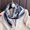 A silk scarf with a blue and white floral print is tied around the neck, displayed against a beige blazer.