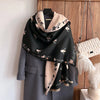A black pashmina shawl with a floral print draped over a gray blazer, displayed against a wooden background.