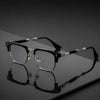 Une paire de lunettes vintage noires à demi-monture avec des accents dorés, posées sur une surface sombre et réfléchissante.
