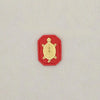 A small, gold-colored turtle charm set within a red, hexagonal-shaped fabric pouch.