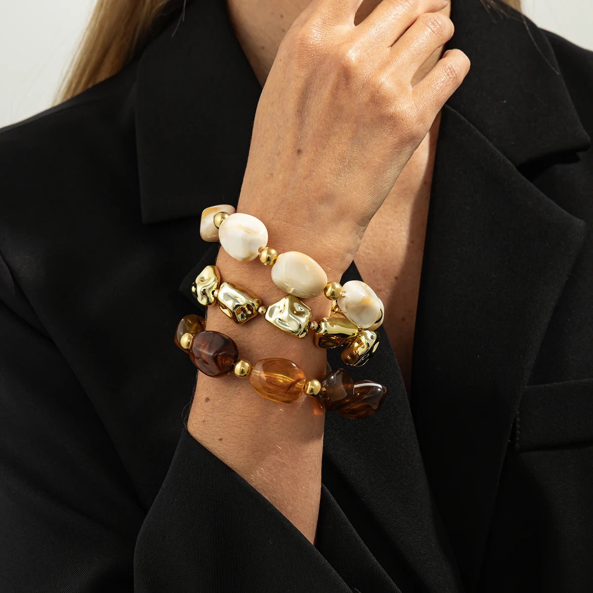 Gros plan d'une main portant un ensemble de bracelets vintage en résine acrylique bohèmes avec des perles blanches et dorées.
