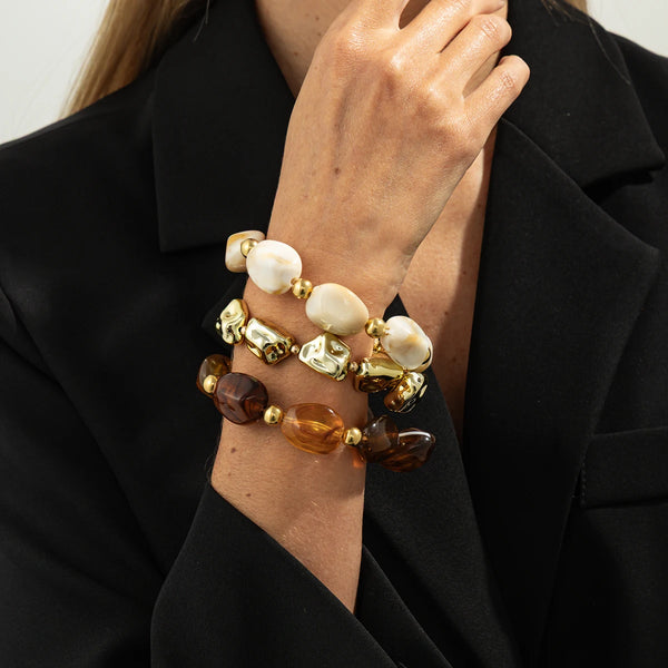 A close-up of a hand wearing a set of bohemian acrylic resin vintage charm bracelets featuring white and gold beads.