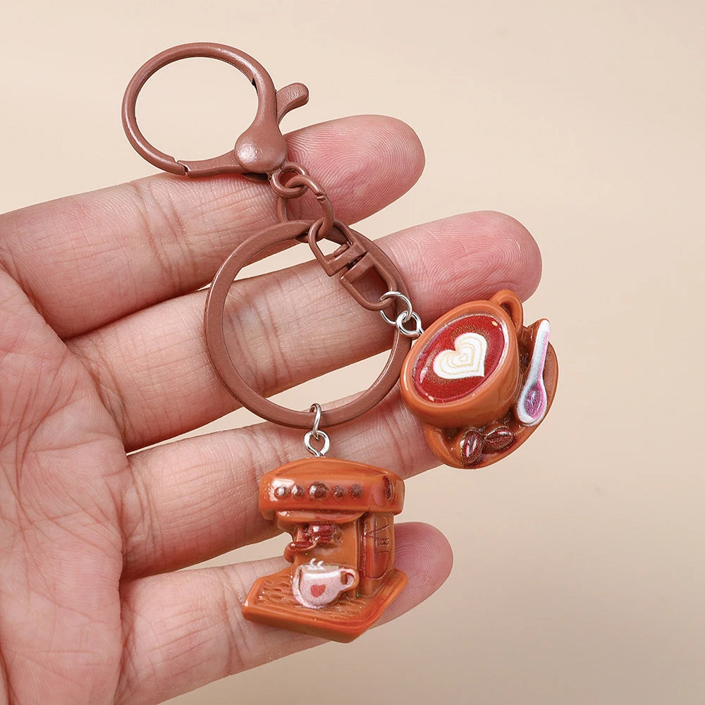 A hand holds a brown leather coffee keychain featuring a small heart-shaped cup and a miniature coffee pot.
