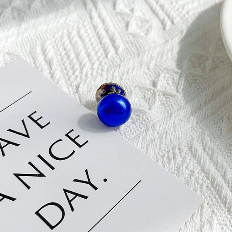 A close-up of a blue pearl button set with silver findings resting on a white card against a textured white background.
