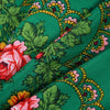 A close-up of a luxury floral print square scarf in shades of green, pink, and yellow on a silk fabric.