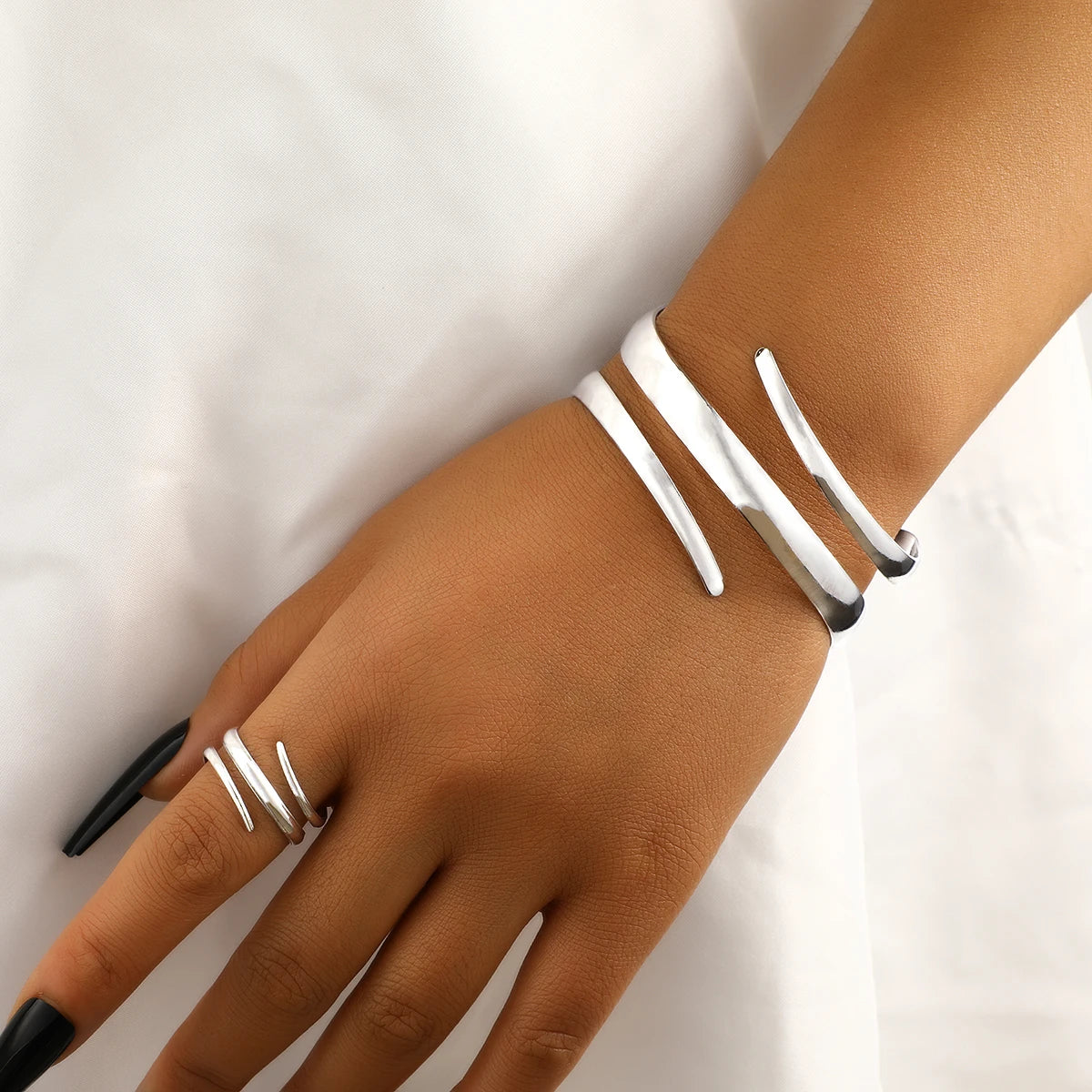 Gros plan d'une main portant un ensemble de bracelets et bagues géométriques en or sur le poignet et les doigts.