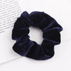A close-up of a dark navy velvet scrunchie with ruffled texture lying on white paper.