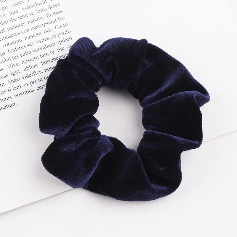A close-up of a dark navy velvet scrunchie with ruffled texture lying on white paper.