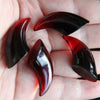 A hand holds several polished, dark red to black silicone molds shaped like devil horns and claws.