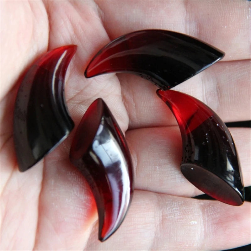 A hand holds several polished, dark red to black silicone molds shaped like devil horns and claws.
