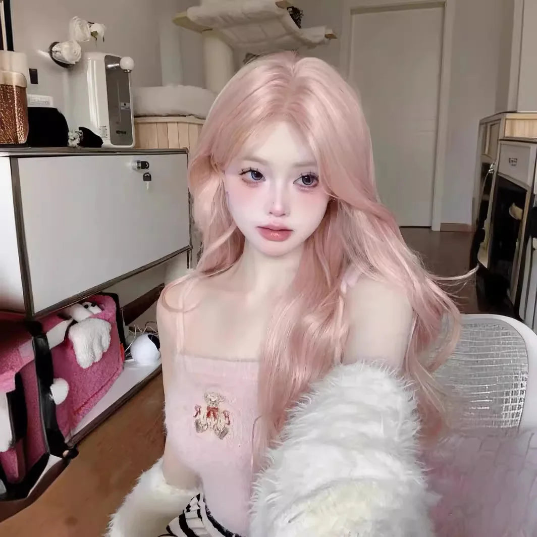 Primer plano de una mujer modelando una peluca sintética larga y rizada rosa rosa con flequillo, vistiendo un top rosa claro 