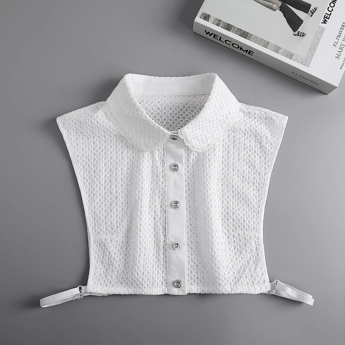 White knitted blouse with a false collar and buttons displayed on a gray background.