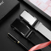 A black smartwatch and leather strap are displayed on a dark surface next to a pen.