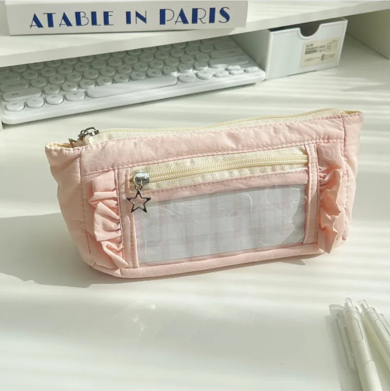 A pink lace pencil case with a clear window and decorative stitching is displayed on a white surface.