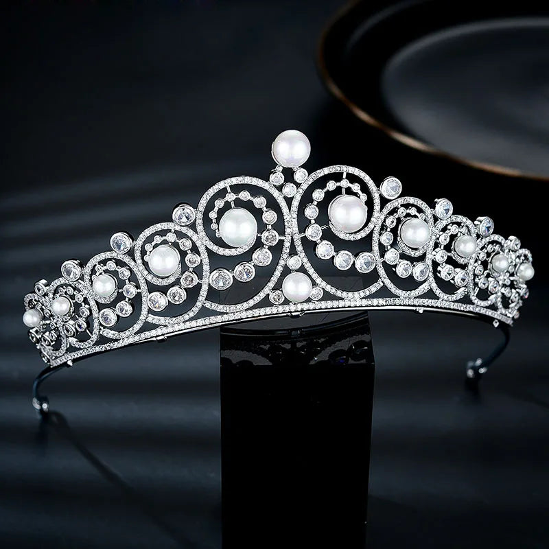 A sparkling cubic zirconia bridal tiara headband with white pearls and clear stones displayed on a dark surface.