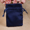 A dark navy satin drawstring pouch with blue ties resting on a beige fabric next to pink flowers.