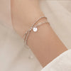 A close-up of a sterling silver double heart charm bracelet worn on a wrist against a light background.